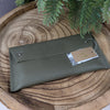 Green leather wallet with a tag on a wooden surface with green leaves.