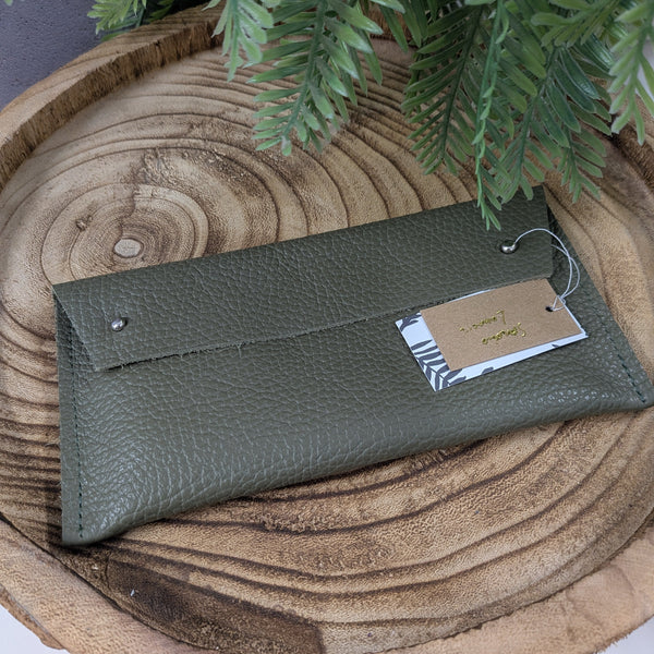 Green leather wallet with a tag on a wooden surface with green leaves.