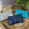 Collection of small leather pouches in various colors on a wooden surface with a plant in the background.