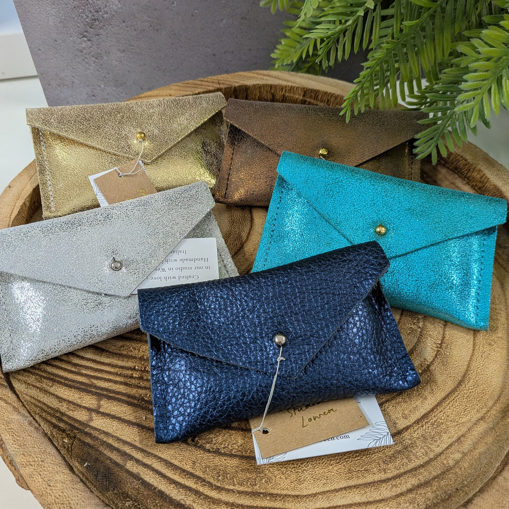 Collection of small leather pouches in various colors on a wooden surface with a plant in the background.