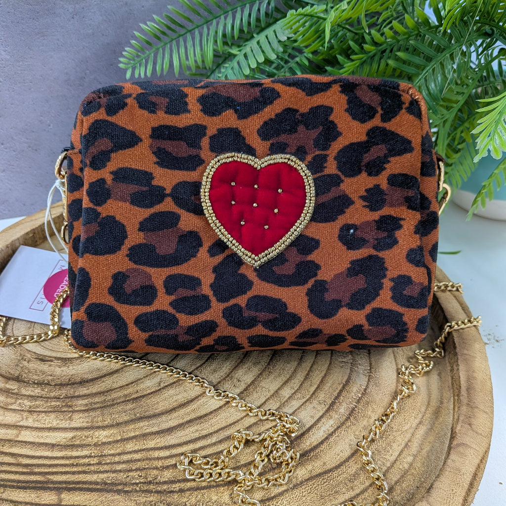 Leopard print handbag with a red heart and gold chain on a wooden surface.