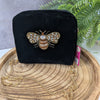 Black velvet handbag with a bee embellishment on a wooden surface with a plant in the background