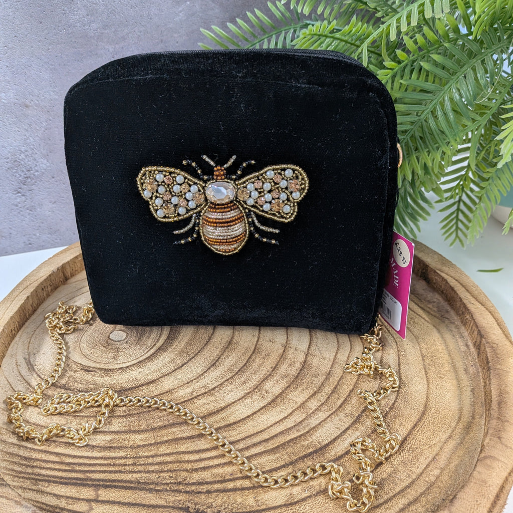 Black velvet handbag with a bee embellishment on a wooden surface with a plant in the background