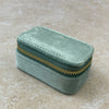 A small rectangular mint green velvet zipper case with a gold zipper, resting on a textured beige stone surface.