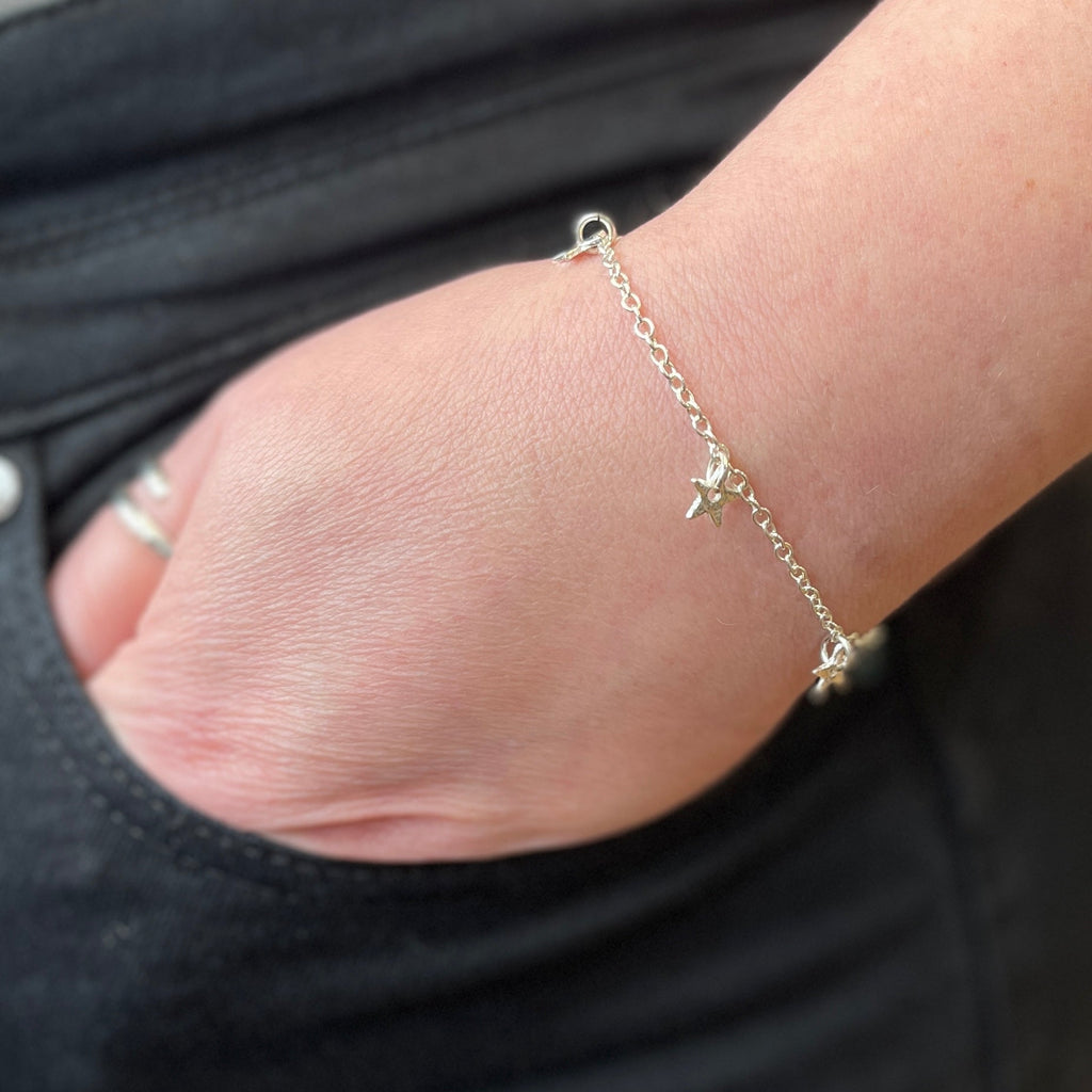 Close-up of a wrist wearing a delicate sterling silver star bracelet with a blurred background