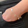 Close-up of a wrist wearing a delicate silver bracelet with small textured circle charms against a dark background.