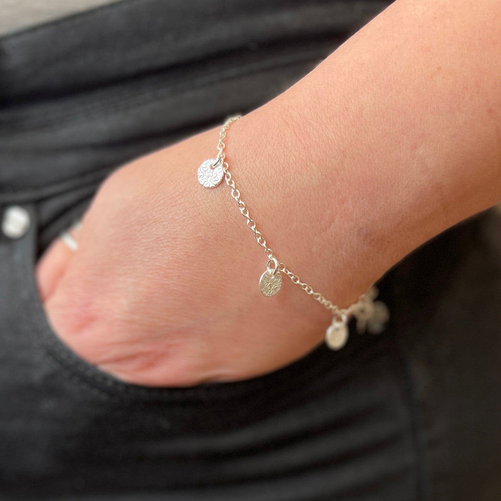 Close-up of a wrist wearing a delicate silver bracelet with small textured circle charms against a dark background.