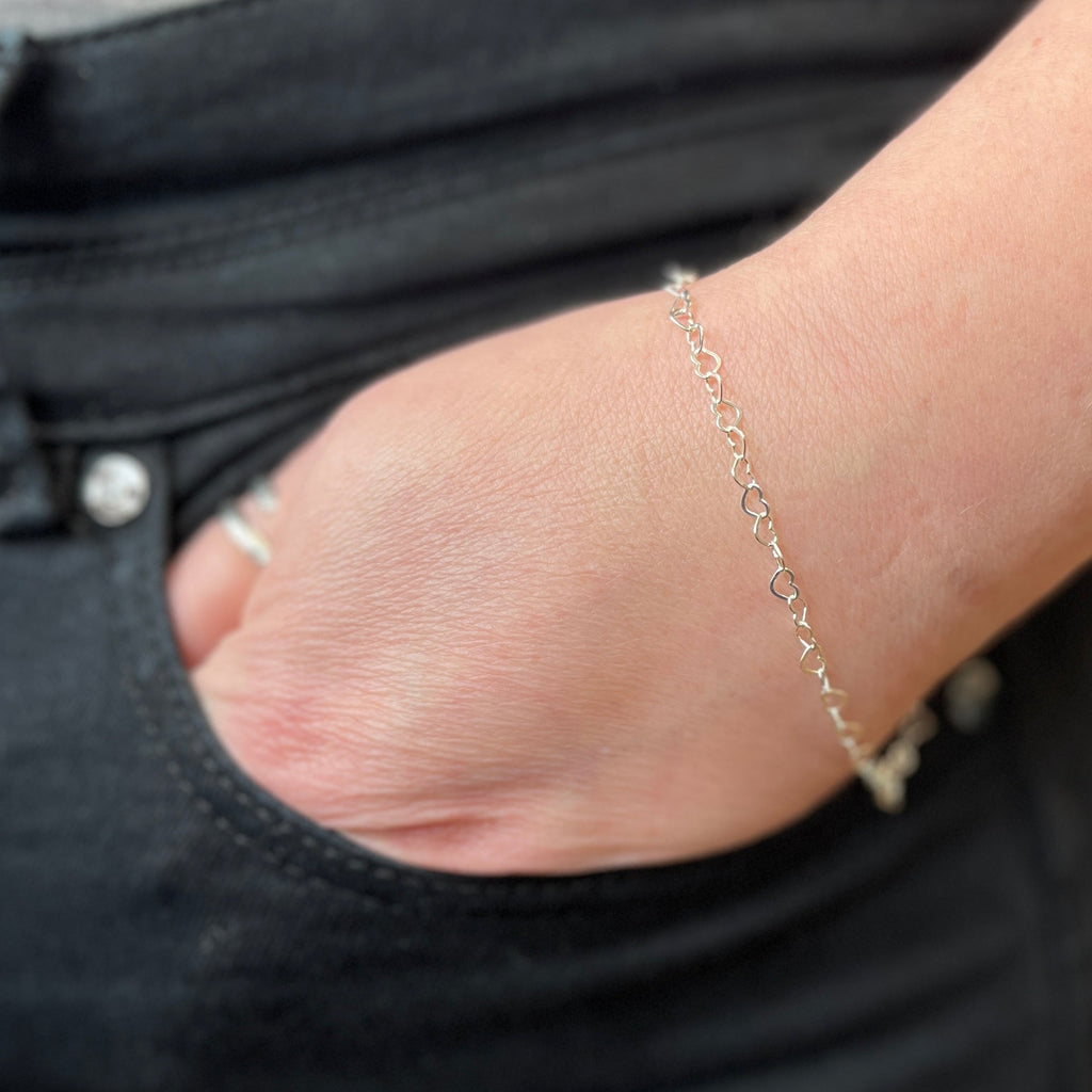 Close-up of a hand wearing a delicate heart chain bracelet with a blurred background