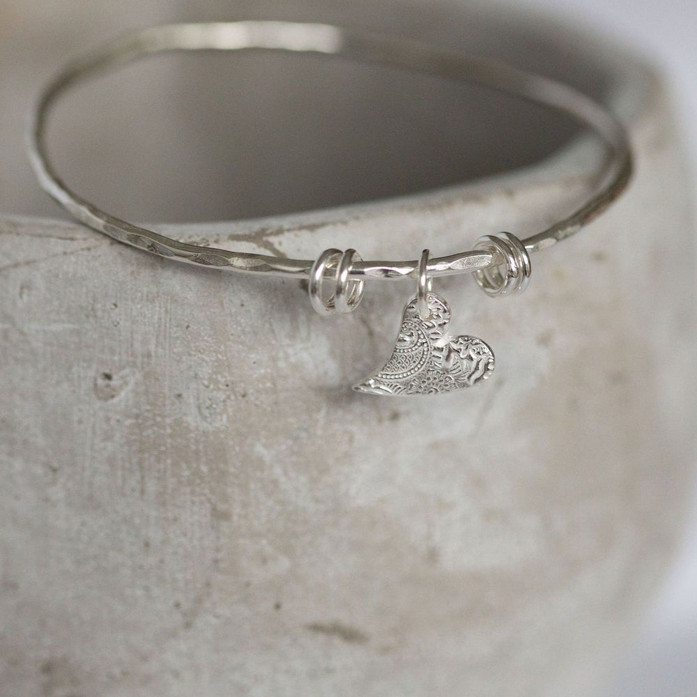 
                  
                    sterling silver delicately textured tilted heart charm bangle by Lucy Kemp Jewellery in Cornwall
                  
                