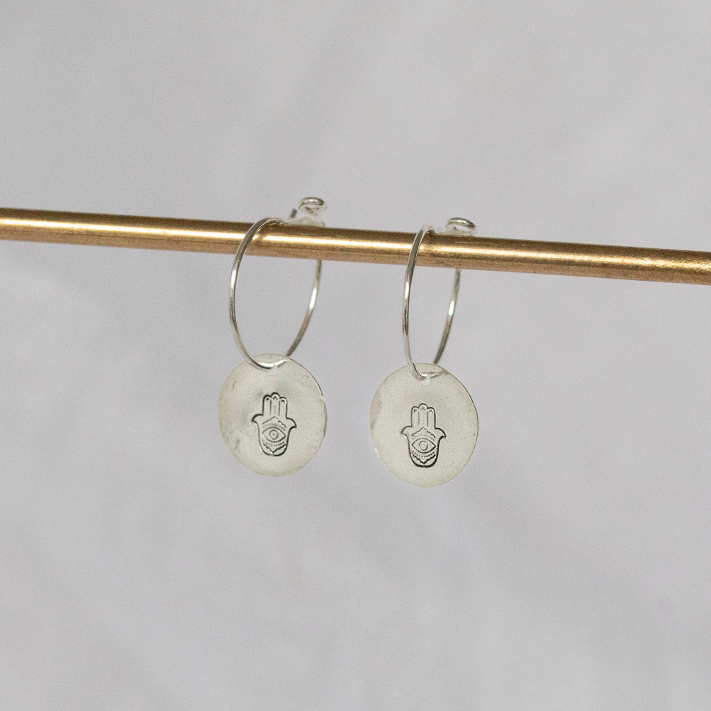 
                  
                    Sterling silver hamsa hand stamped charm hoops by Lucy Kemp Jewellery 
                  
                