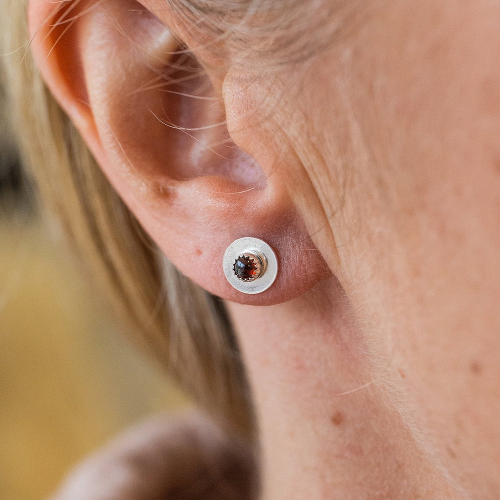 
                  
                    Worn Garnet and sterling silver birthstone small disc studs by Lucy Kemp Jewellery
                  
                