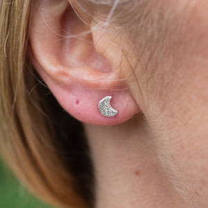 
                  
                    sterling silver textured mini mismatch moon and star studs, moon worn, by Lucy Kemp Jewellery 
                  
                